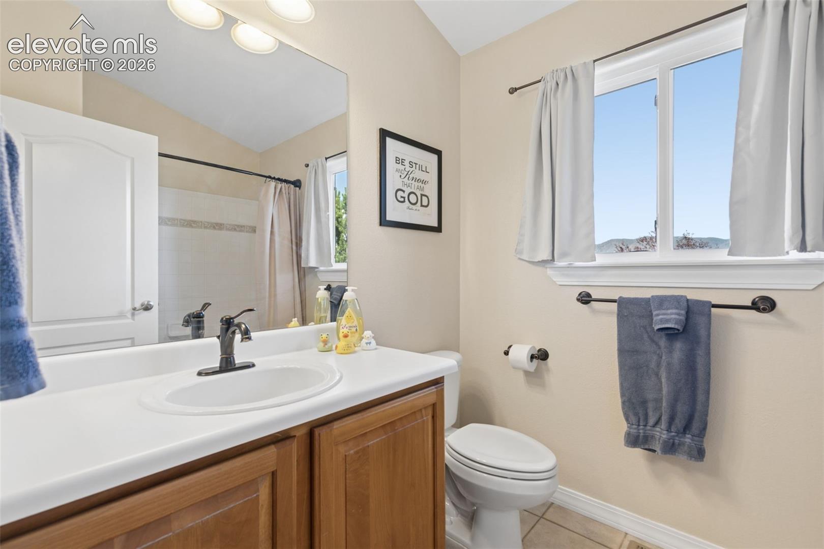 Bathroom featuring a wood-finish vanity with an integrated sink, broad wall mirror, and a window for natural light