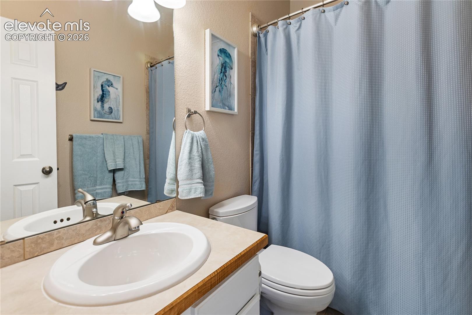 Bathroom featuring a vanity with an integrated sink, a large mirror, a toilet, and a shower curtain on a rod