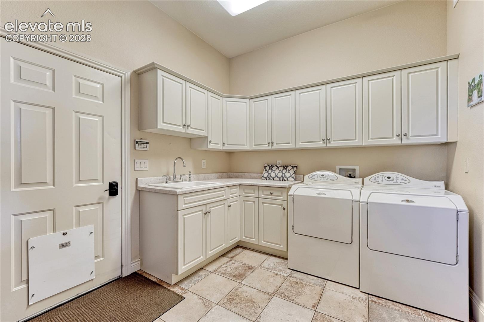 Laundry area featuring custom white cabinetry, stone-finish countertops, an integrated utility sink, and stone-tile flooring