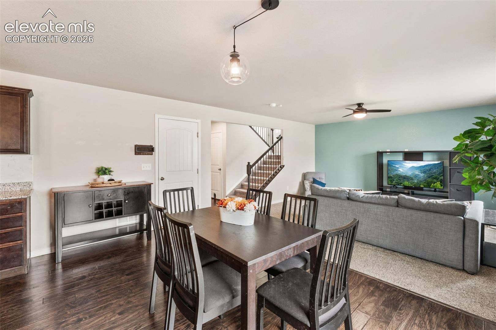 Wood-finish flooring, staircase with dark wood railings, light neutral wall paint, accent wall in a soft blue-green hue, and a ceiling fan with integrated lighting