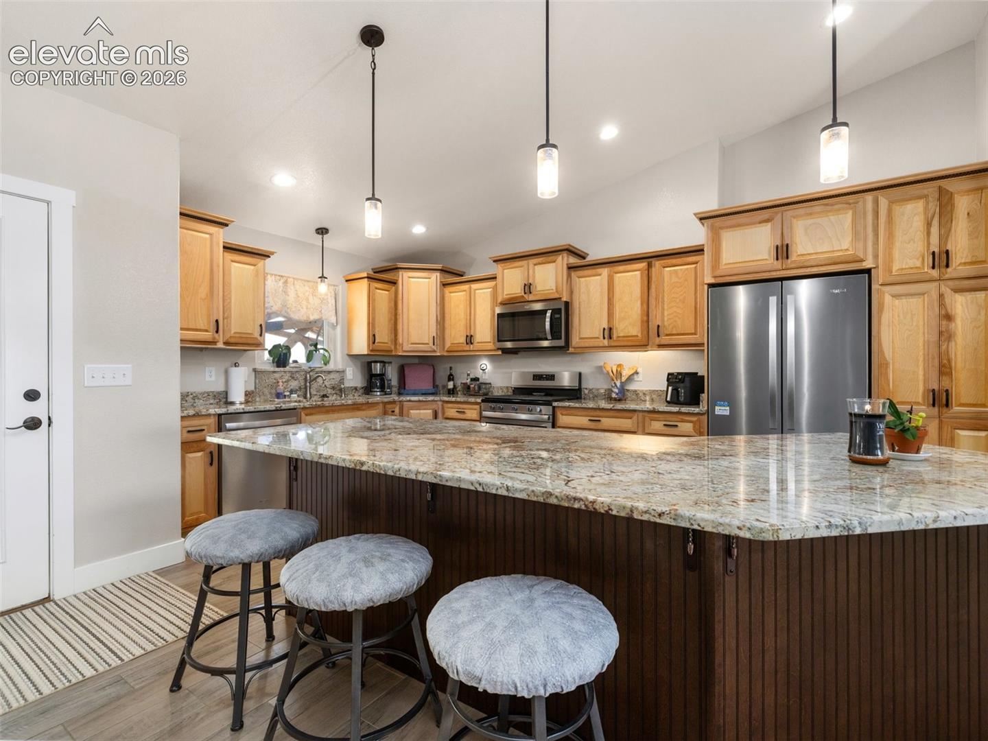 Kitchen featuring light wood cabinetry, stainless steel appliances, a large island with a stone-finish countertop, and recessed lighting