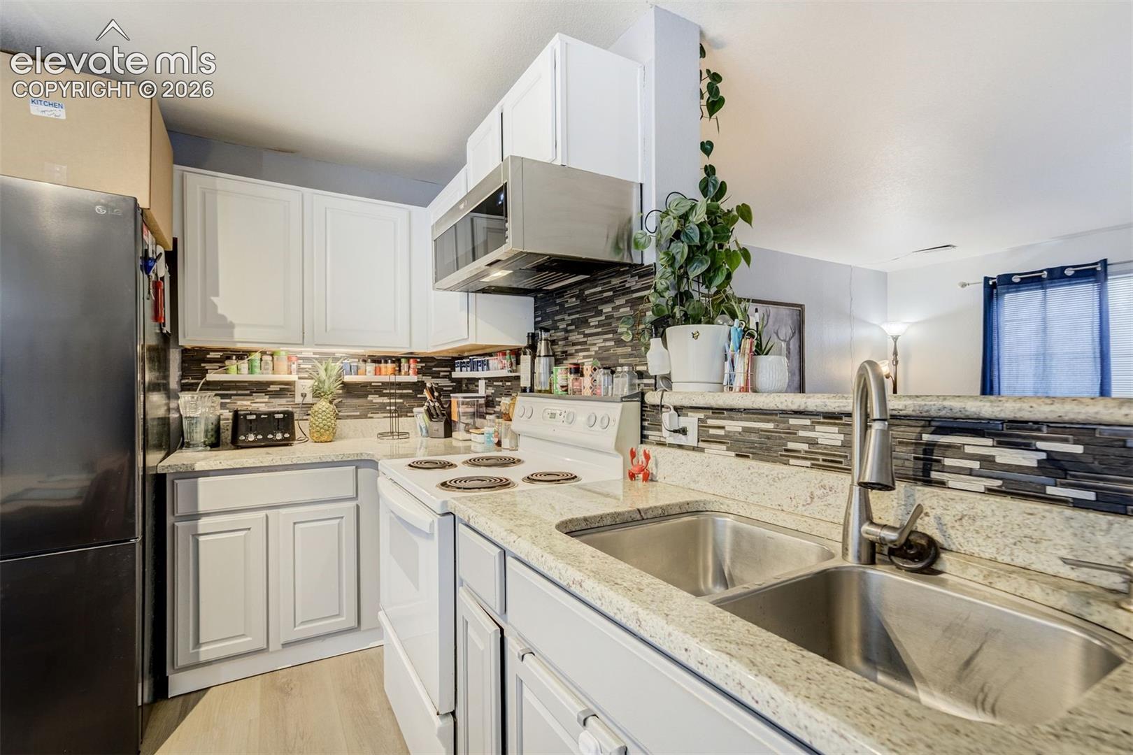Kitchen featuring white cabinetry, stone-finish countertops, stainless steel double basin sink with gooseneck faucet, microwave, and a tile backsplash
