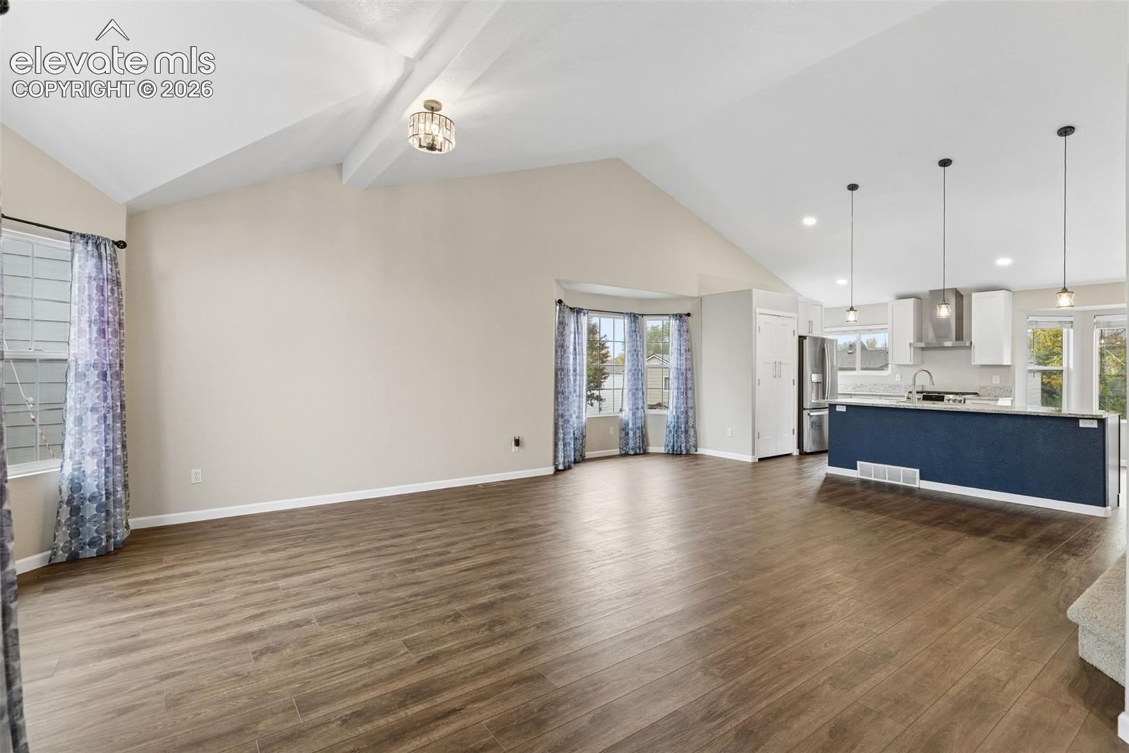 Vaulted ceilings with exposed beams, wood-finish flooring, kitchen island with matte-finish base cabinetry, recessed lighting, and bay window