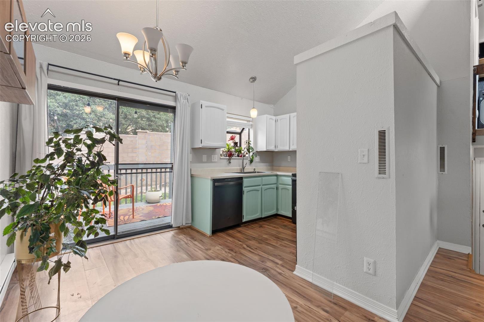 Vaulted ceiling, wood-finish flooring, sliding glass door, kitchen with dishwasher, and upper/lower cabinetry