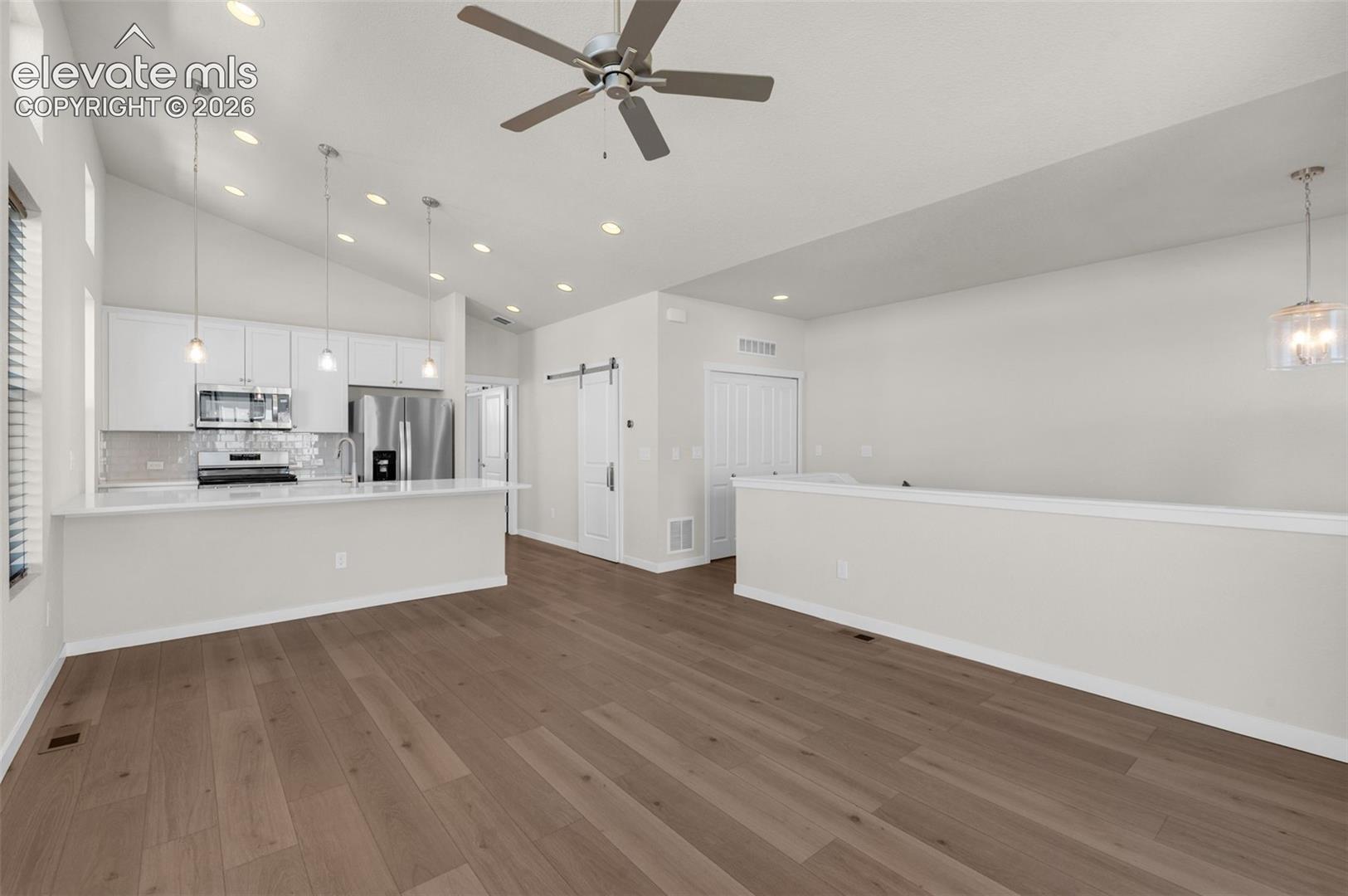 Vaulted ceilings with recessed lighting, wood-finish flooring, white cabinetry, a peninsula with stone-finish countertops, and a sliding barn door