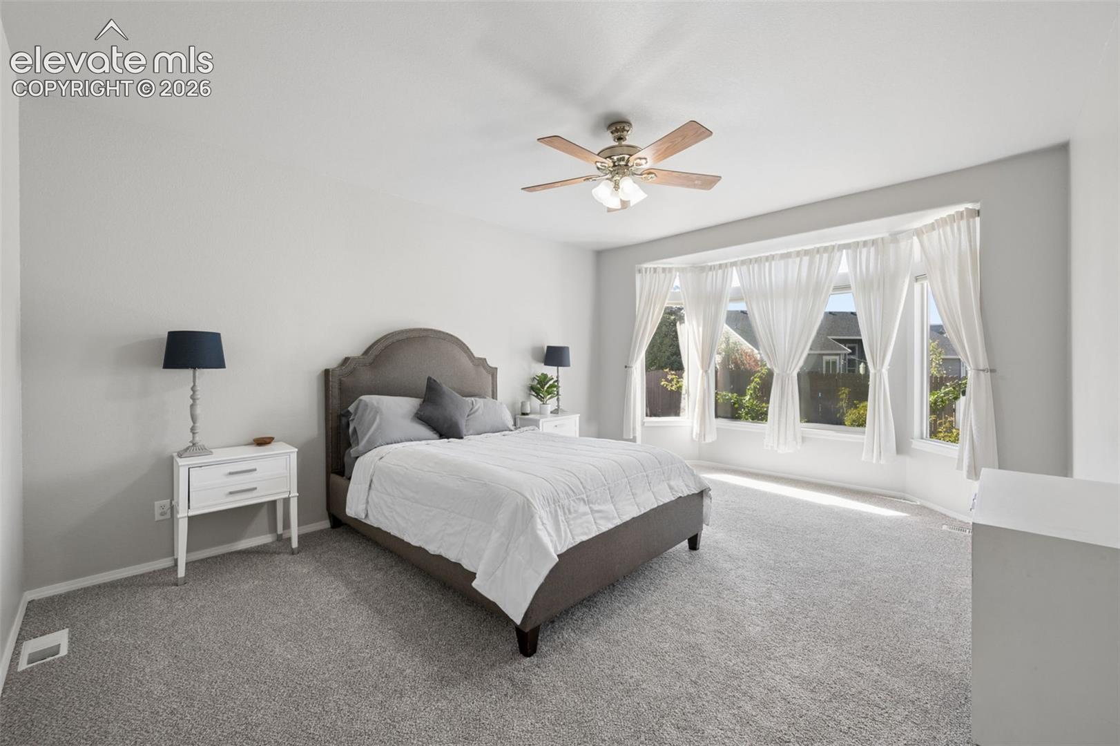 Neutral-toned carpeting, bay window, and a central ceiling fan with integrated lighting