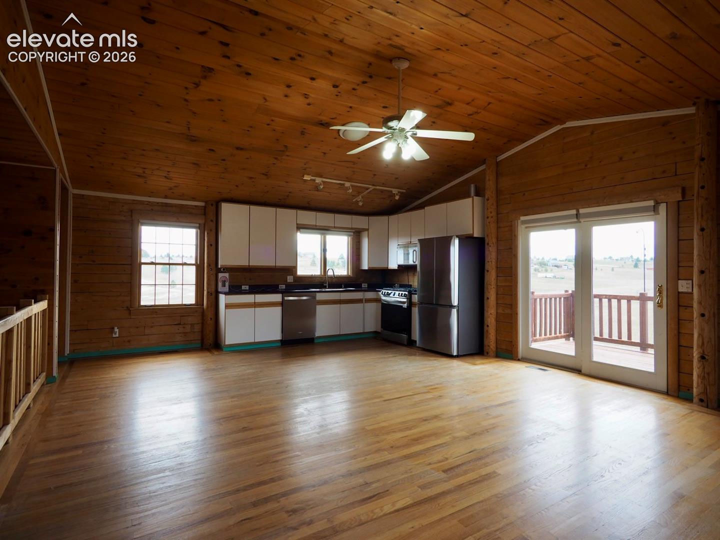 Vaulted wood-plank ceiling, wood-finish flooring, log-style wall detailing, stainless steel appliances, and sliding glass doors with exterior deck access
