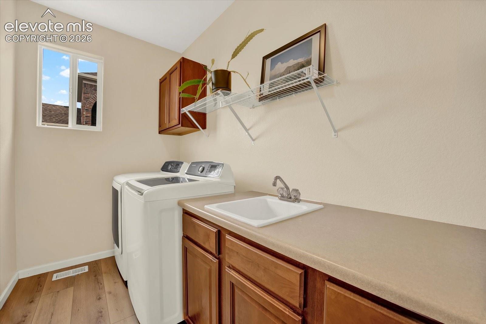 Utility space featuring wood-finish flooring, wood-toned cabinetry, a solid-surface countertop with an integrated drop-in sink, and wire shelving