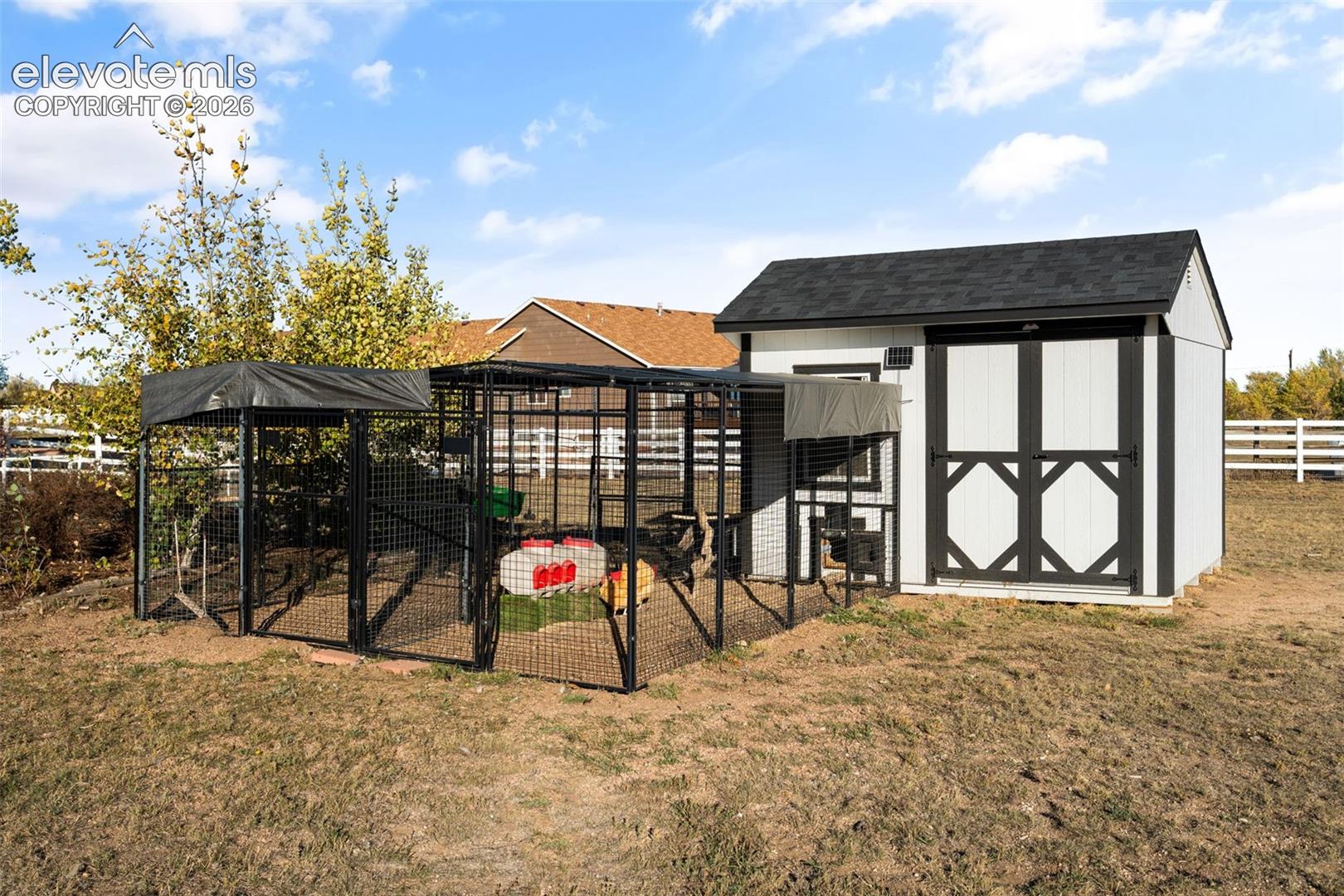 Detached exterior structure featuring a gabled asphalt-shingle roof, wood-panel siding, double-door access, and an attached, fenced-in metal mesh enclosure