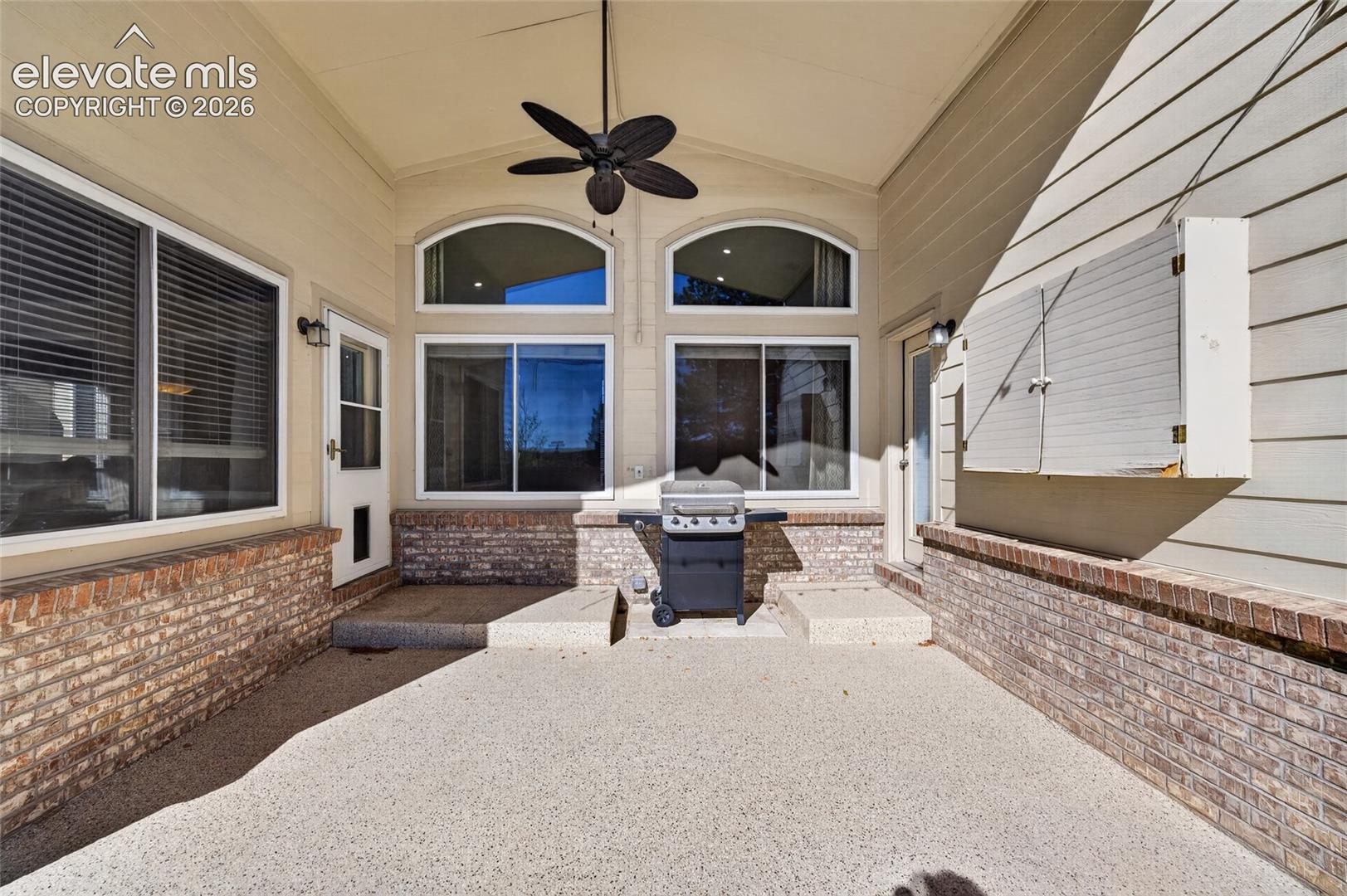 Covered patio featuring aggregate concrete flooring, brick wainscoting, ceiling-mounted fan, and arched windows