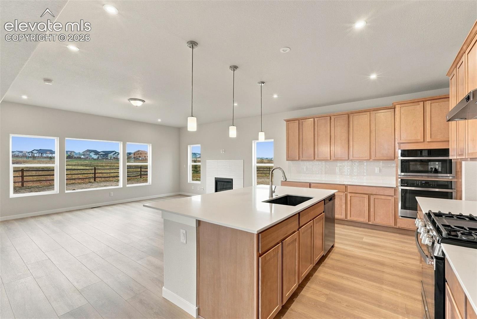 Kitchen featuring light wood cabinetry, quartz countertops, a central island with an undermount sink, built-in double wall ovens, and wood-finish flooring