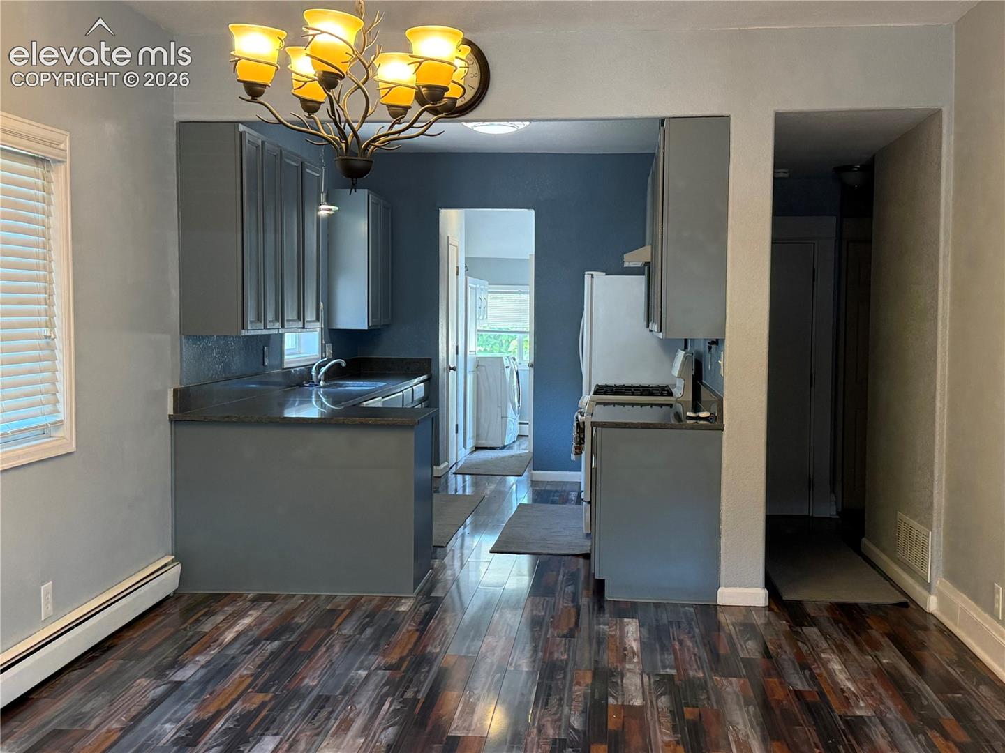 Kitchen featuring dark-toned cabinetry, solid surface countertops, multi-tonal wood-finish flooring, and an ornamental metal chandelier