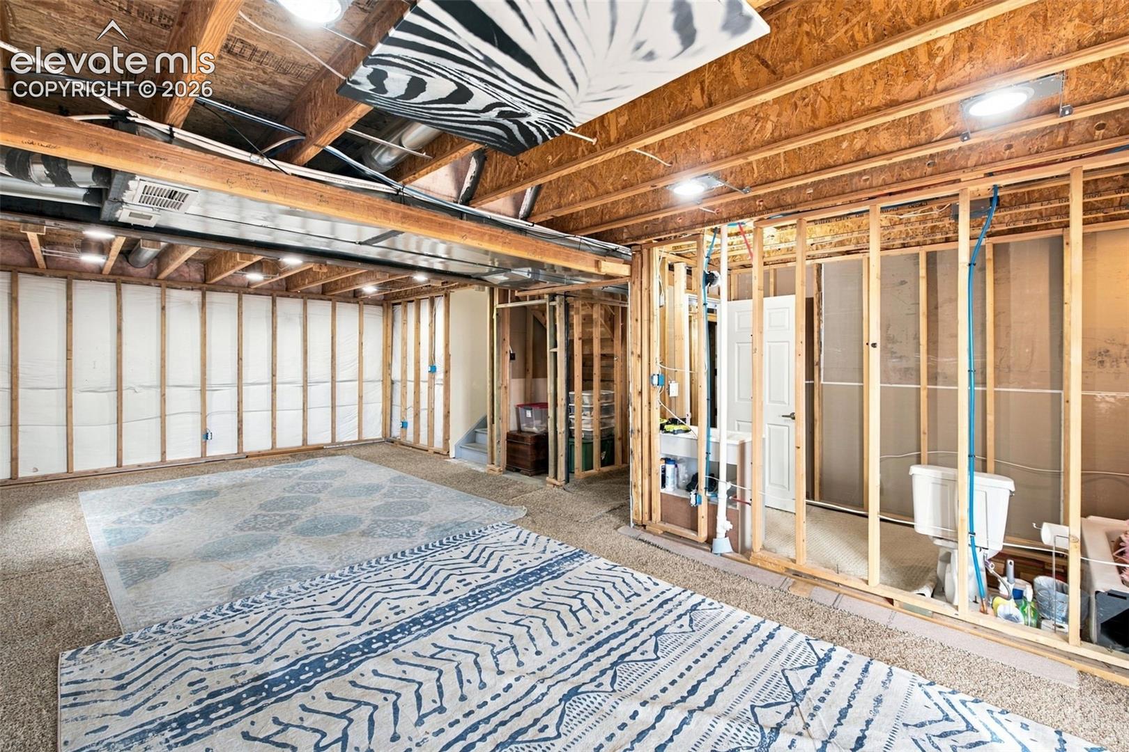 Unfinished lower level featuring exposed wood framing, ceiling joists, recessed lighting, installed plumbing rough-ins, and a pre-installed toilet