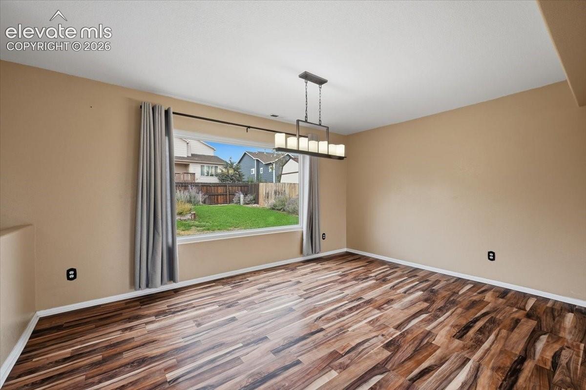 Spacious room featuring wood-finish flooring, a large window, and a linear chandelier