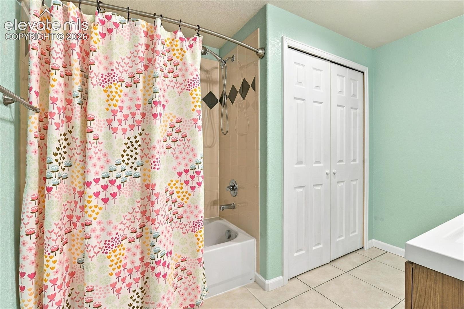 Lower level bathroom featuring a shower-tub combination with patterned tile inlay, double-door closet, and tile flooring