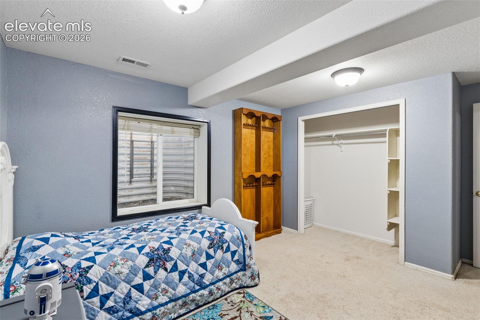 Room featuring neutral carpeting, a large recessed window with a metal window well, built-in wooden shelving, and a walk-in closet with integrated storage cubbies