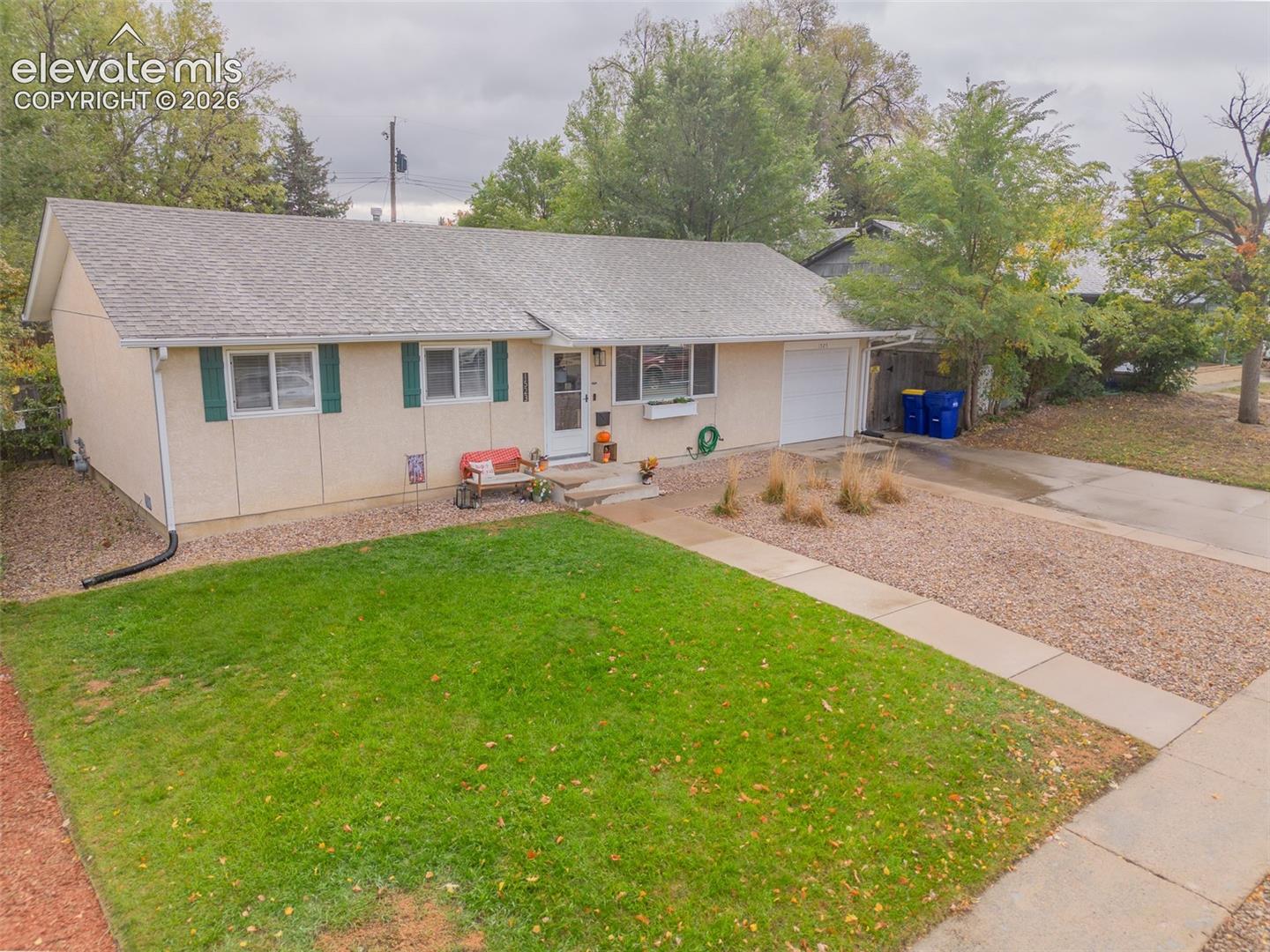 Single-story exterior featuring light-toned siding, a concrete driveway, a gabled roof, an attached garage, and a combination of lawn and decorative rock landscaping