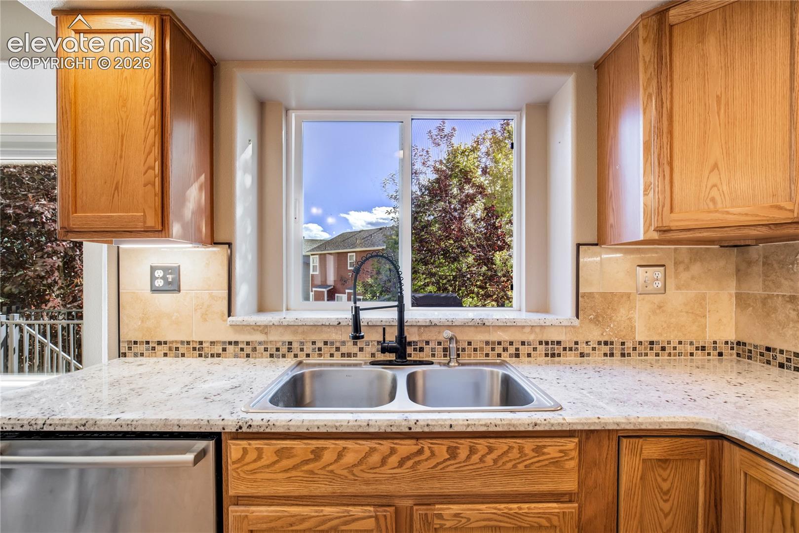 A large window brings natural light to the double-basin sink, with views of the backyard, granite countertops + custom tile backsplash adding to the kitchen's appeal.