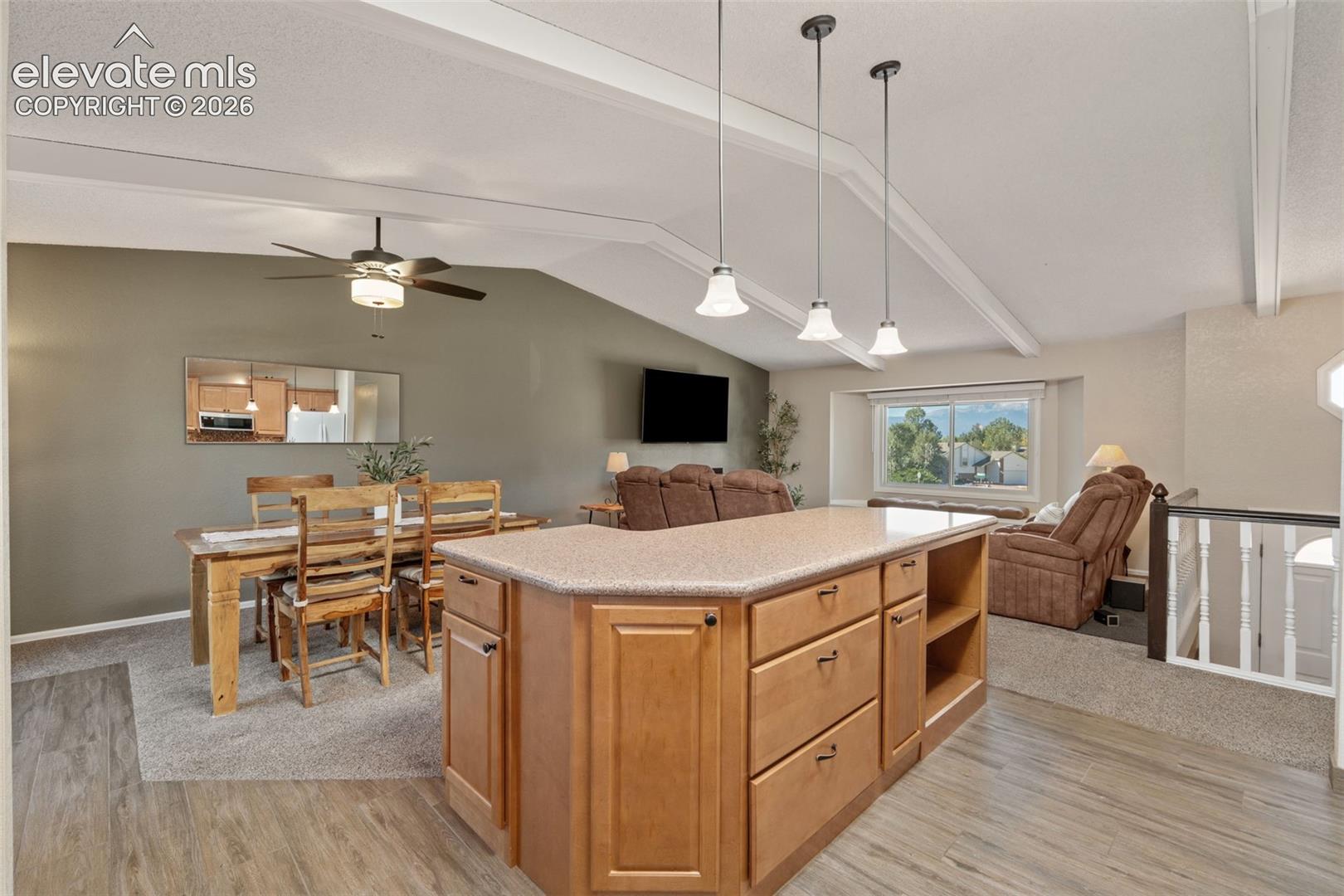 Kitchen island featuring wood cabinetry and a solid-surface countertop, complemented by a trio of pendant lights, vaulted ceilings, and a ceiling fan