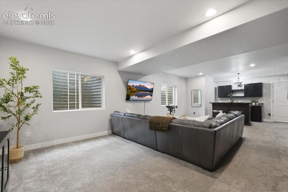 Recessed ceiling lighting, a built-in wet bar with dark cabinetry, wall-mounted television, and a window with white shutters