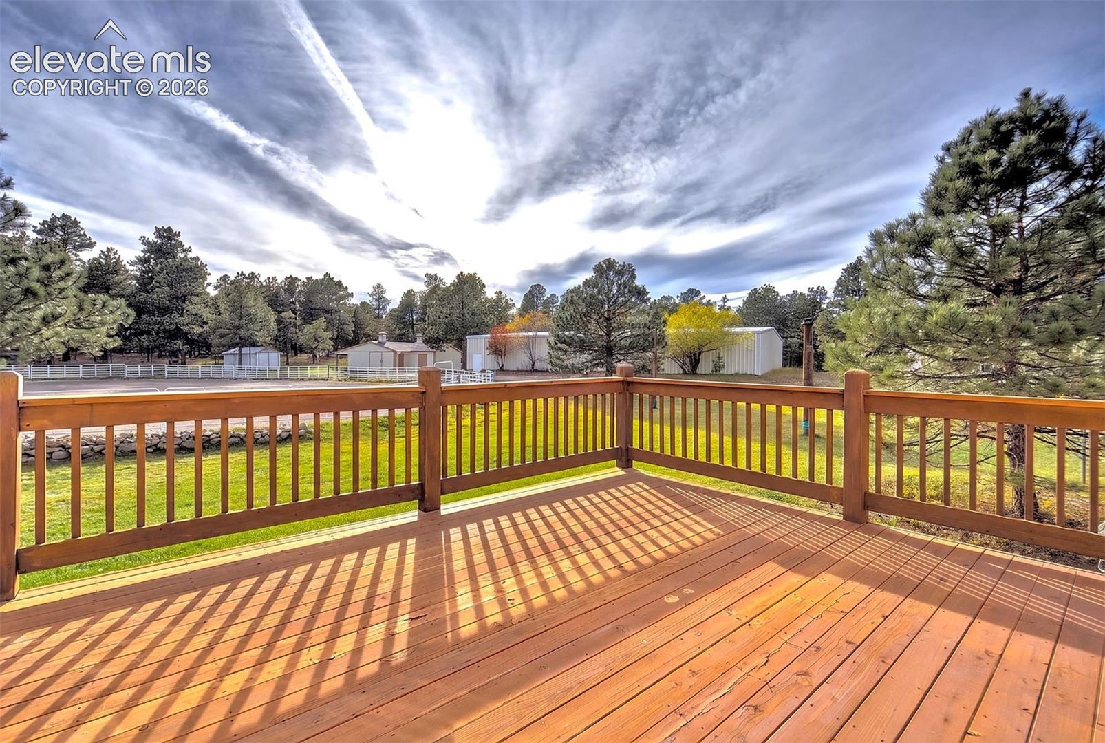 Elevated redwood deck featuring vertical baluster railings and expansive natural surroundings with mature evergreen trees and grass lawn- off of primary bedroom- rebuilt in 2025