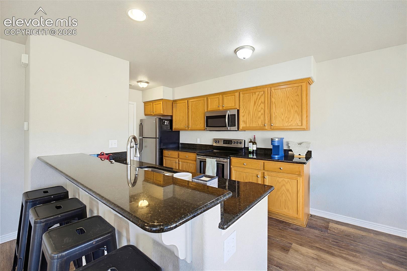 Kitchen featuring dark stone countertops, wood-finish cabinetry, stainless steel appliances, and a breakfast bar