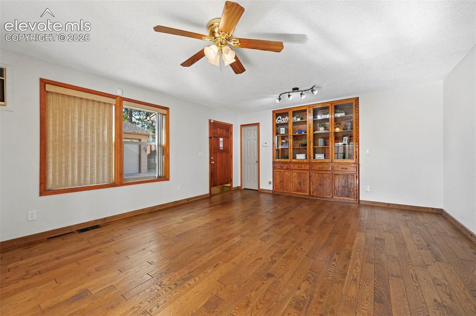 Wood-finish flooring, built-in floor-to-ceiling wooden cabinetry, brass-finish ceiling fan with integrated lighting, and multi-pane window frames