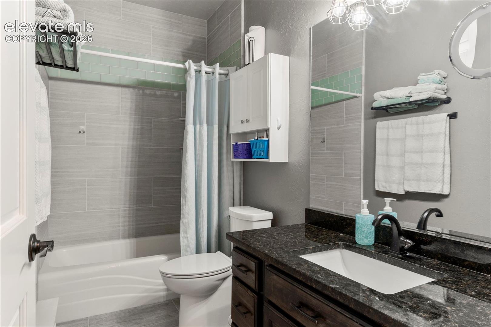 Full bathroom featuring shower / bathtub combination with curtain, a textured wall, and vanity