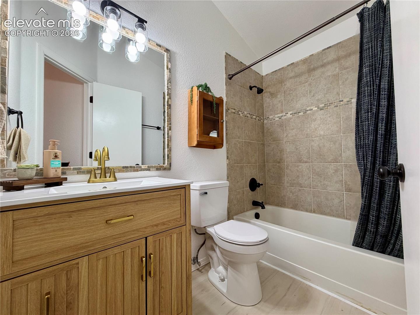 Upstairs guest bathroom featuring a wood-finish vanity with gold-tone hardware, a rectangular undermount sink, and a tiled mirror surround