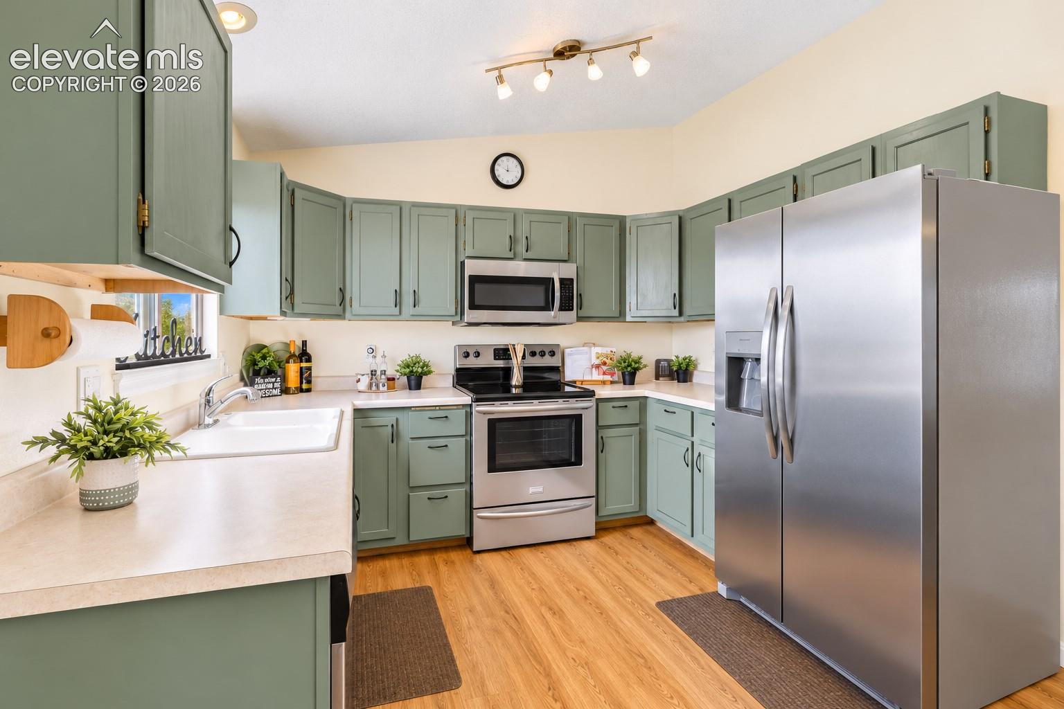 Kitchen featuring sage green cabinetry, stainless steel appliances, wood-finish flooring, solid surface countertops, and an integrated double-basin sink