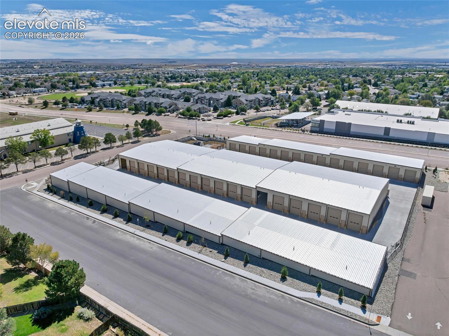 Multiple storage buildings with metal roofs, individual roll-up doors, and paved access areas