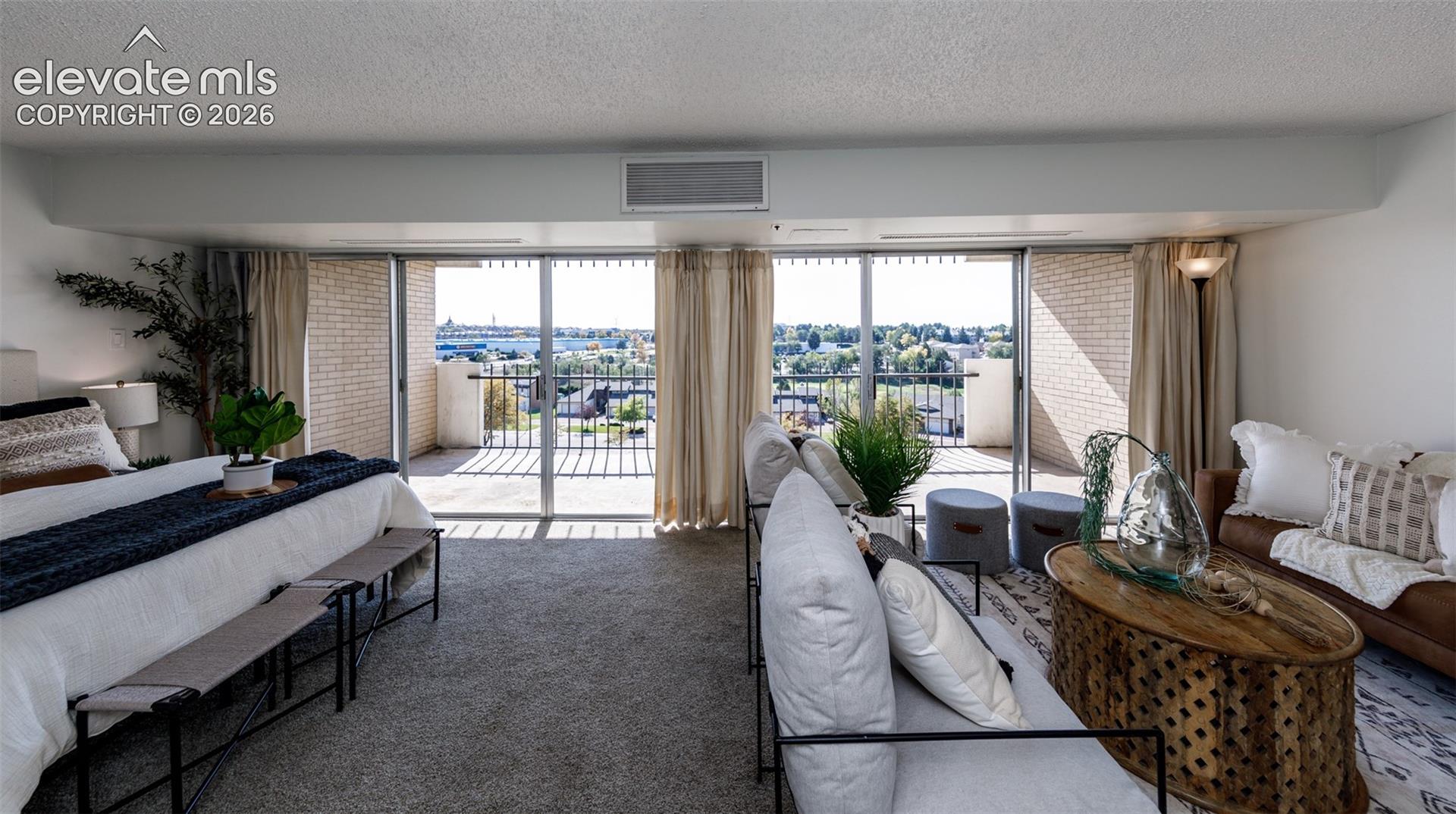 Expansive room with neutral carpeting, floor-to-ceiling sliding glass doors, and a private balcony featuring metal railings and brick masonry walls