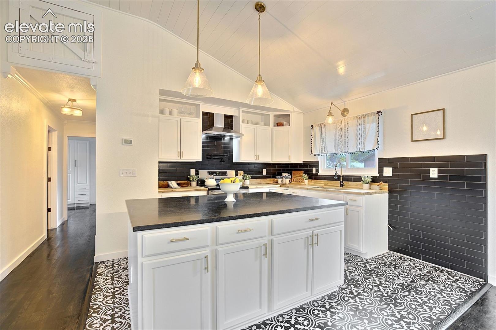 Kitchen featuring white cabinetry, center island with dark countertop, black tile backsplash, pendant lighting, and patterned flooring