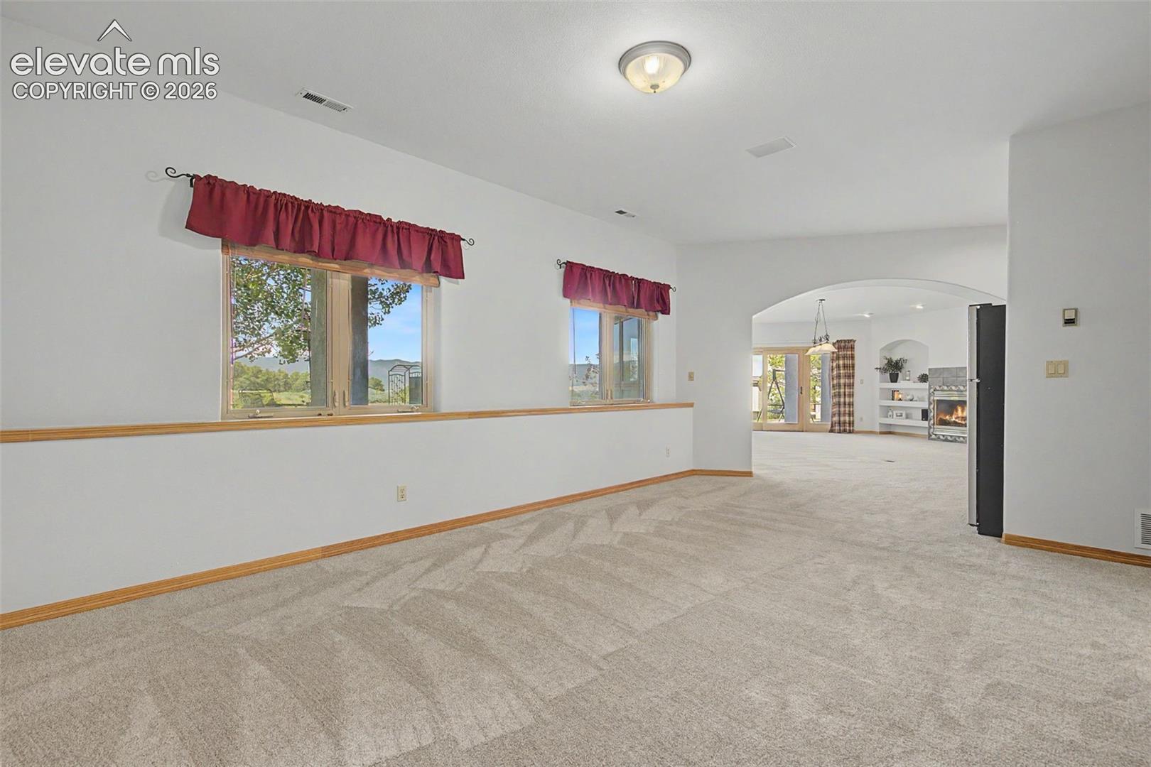 Carpeted interior space featuring two windows, an arched doorway, and light wood-finish trim