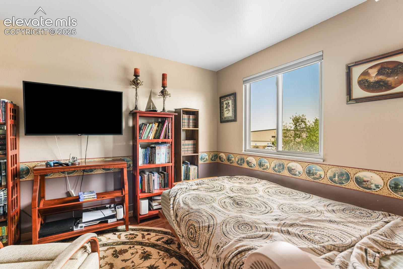 Bedroom featuring a single window with white trim, light beige walls, and wood-finish flooring