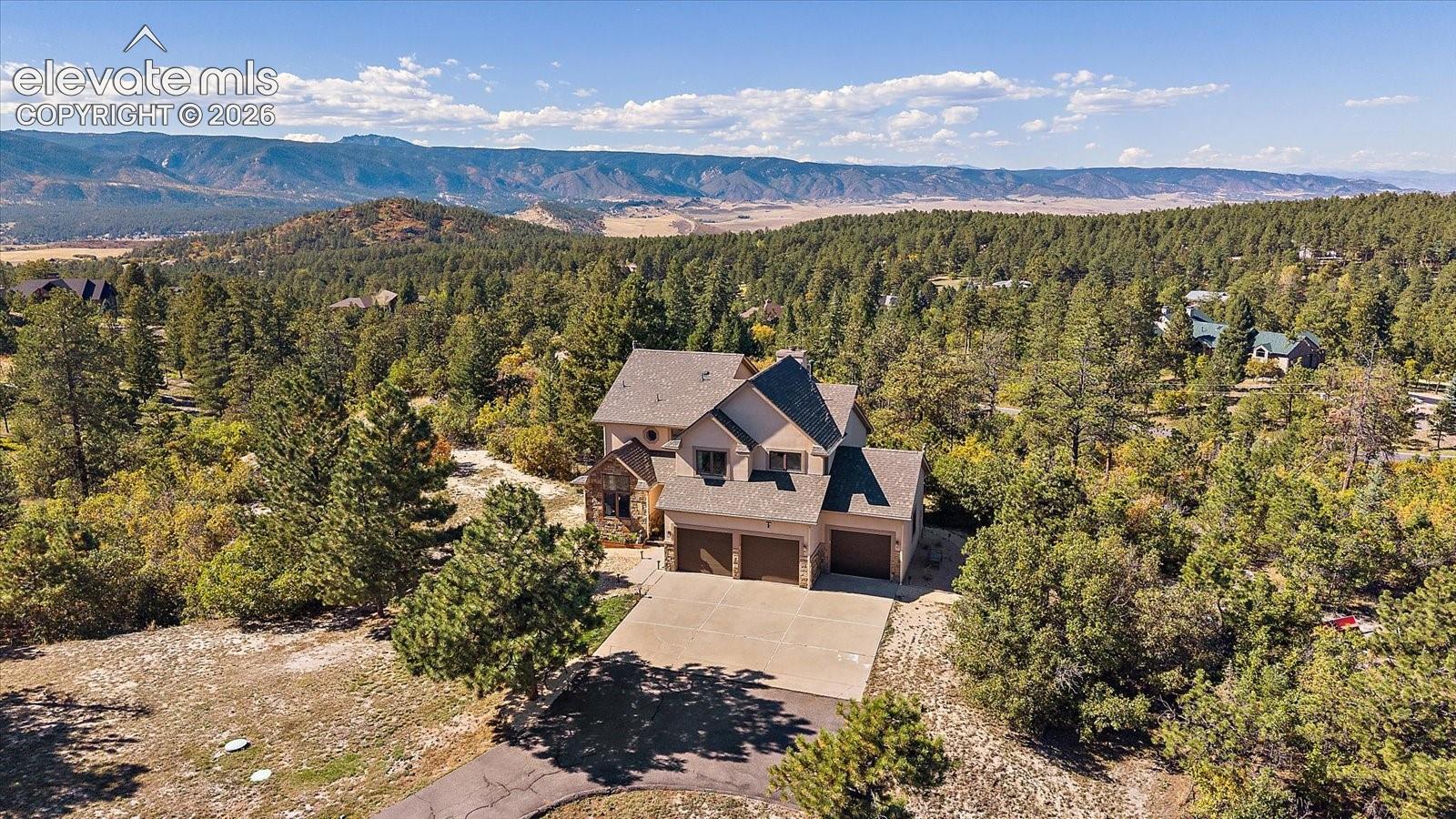 Multi-level residence featuring a multi-car garage, stone and siding exterior, expansive mountain backdrop, and forested surroundings