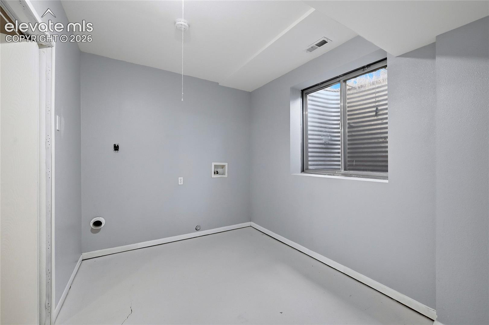 Neutral-toned utility room featuring hookups for laundry appliances, a window with an egress well, and a ceiling-mounted light fixture