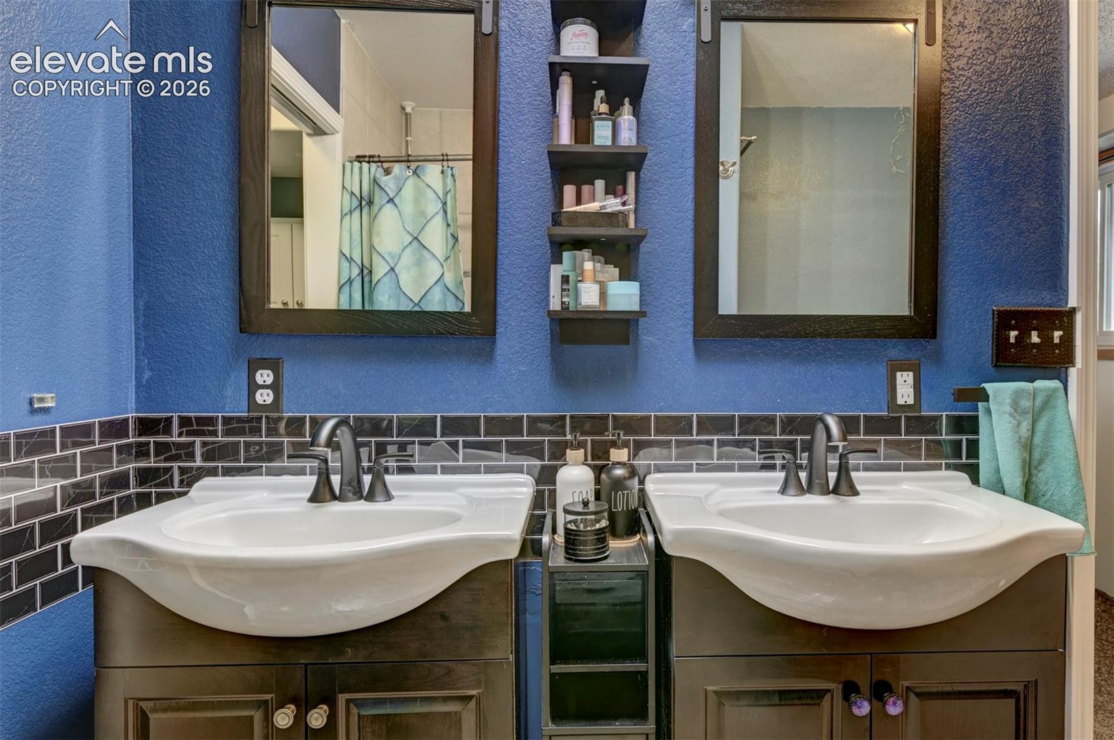 Dual vanity with dark wood-finish cabinetry, black subway tile backsplash, and matte black fixtures