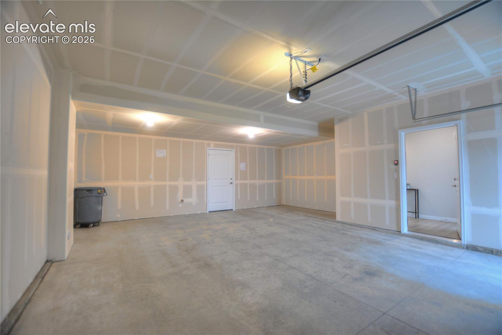 Concrete flooring with two interior doors, overhead lighting, and an automatic garage door opener