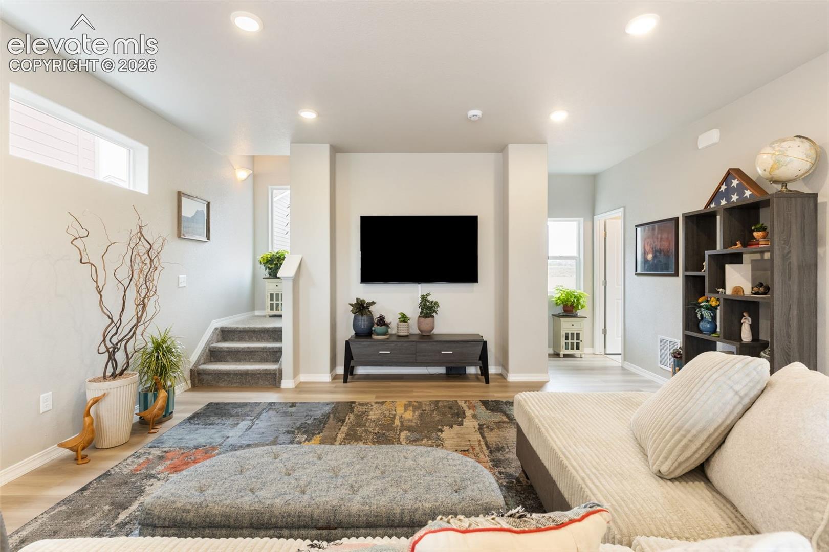 Spacious living area featuring light-toned walls, recessed lighting, and wood-finish flooring