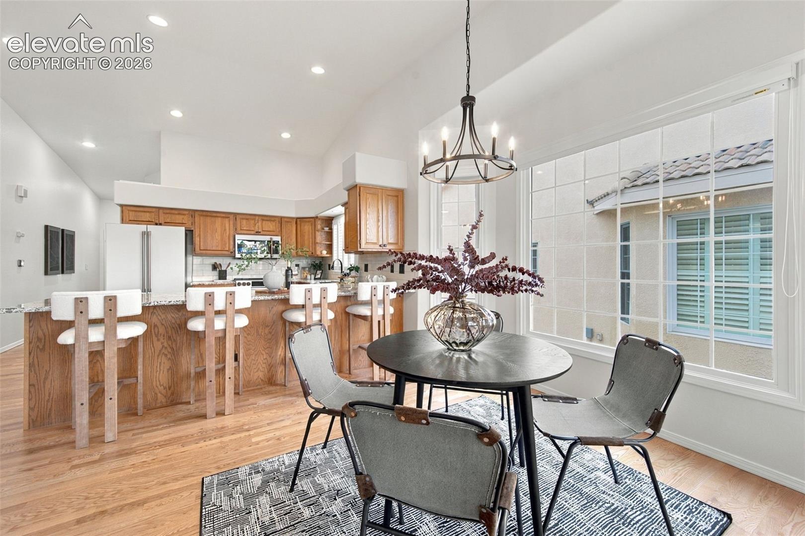 Kitchen featuring wood cabinetry, stone countertops, and recessed lighting, paired with a breakfast nook containing a metal chandelier and large grid-pattern windows