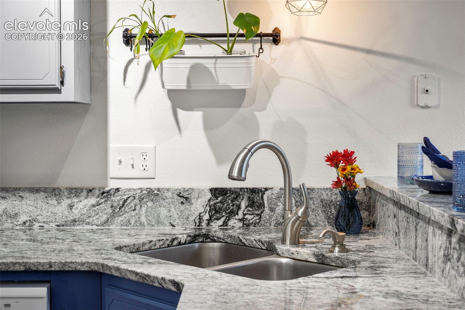Stone countertop with integrated matching backsplash, stainless steel double-basin sink, high-arc pull-down faucet, and custom cabinetry