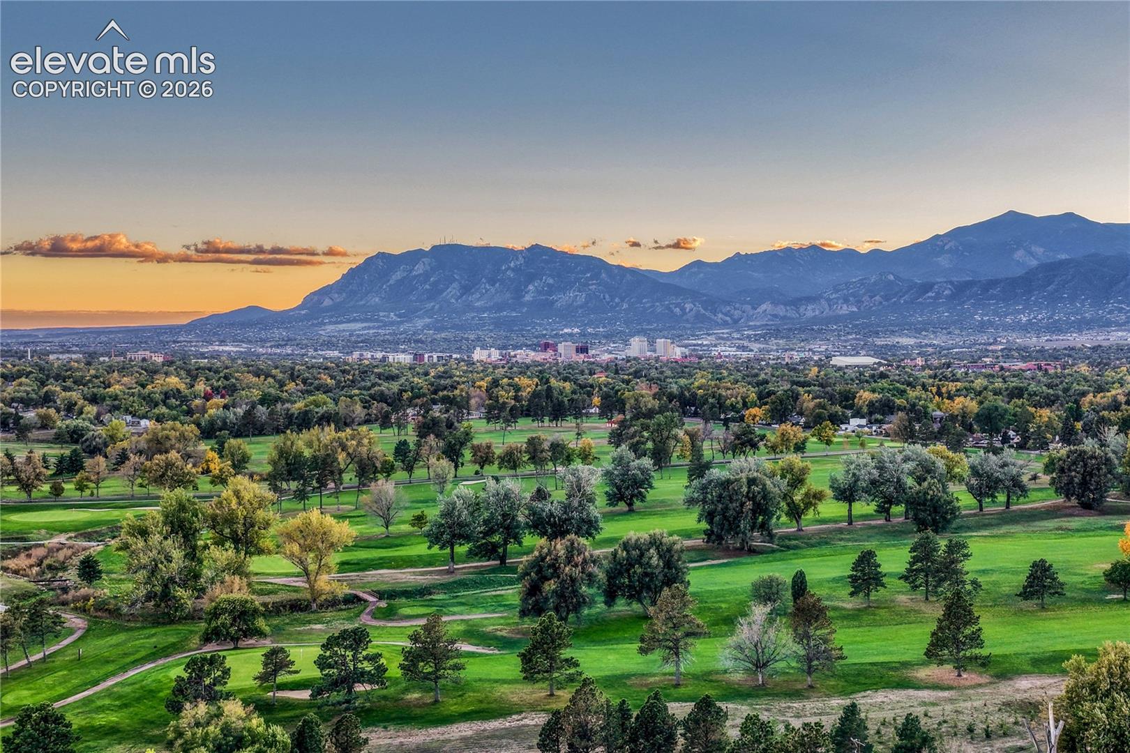 Panoramic landscape featuring mature trees, manicured greens, and mountain range scenery