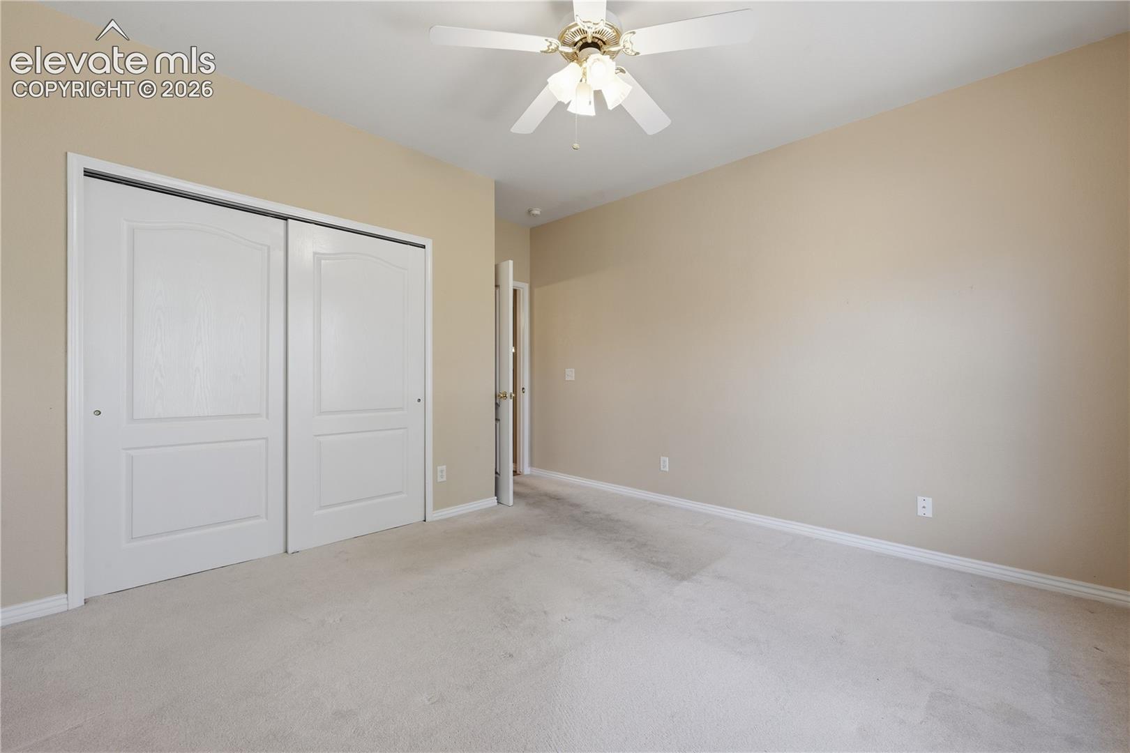 Room featuring carpeting, neutral wall paint, a ceiling fan with integrated lighting, and dual sliding closet doors with arched panel detail