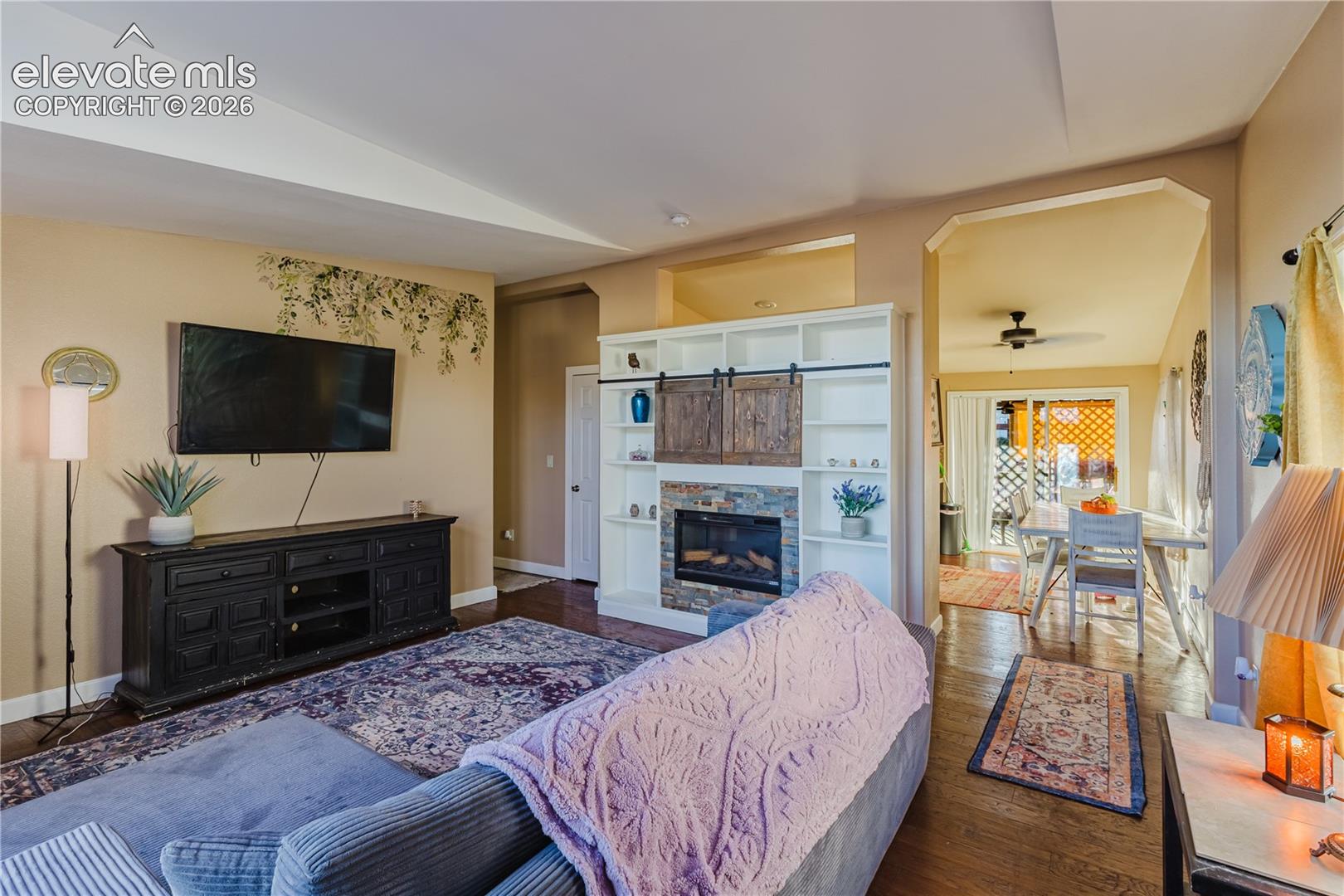 Built-in shelving with barn door accents, stone-faced fireplace, recessed lighting, and wood-finish flooring