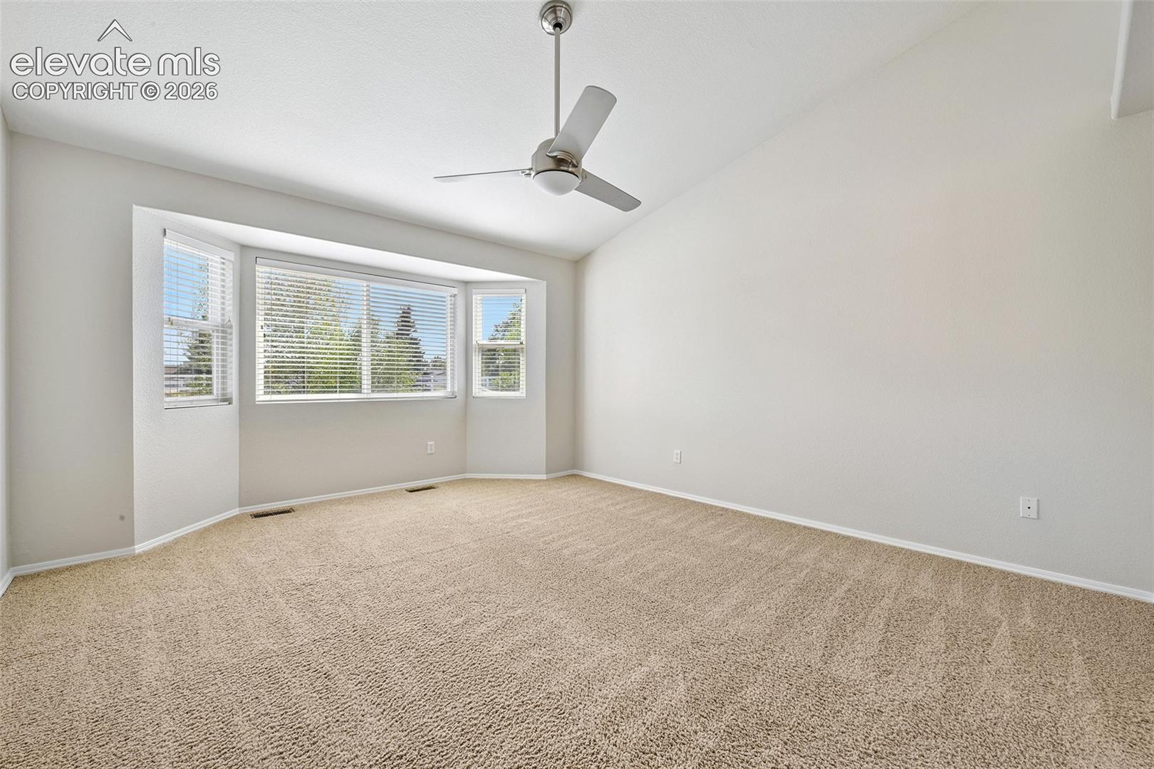 Spacious room featuring vaulted ceilings, a large bay window, neutral carpeting, and a ceiling fan. Could be an office etc. 