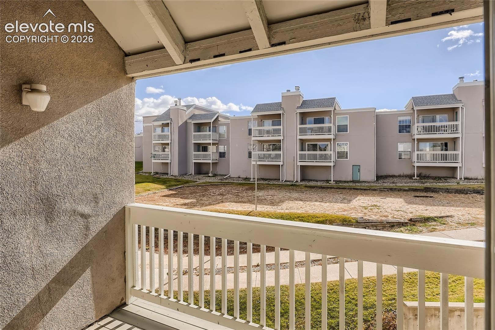 Covered balcony featuring white wood-style railing and exterior wall-mounted lighting