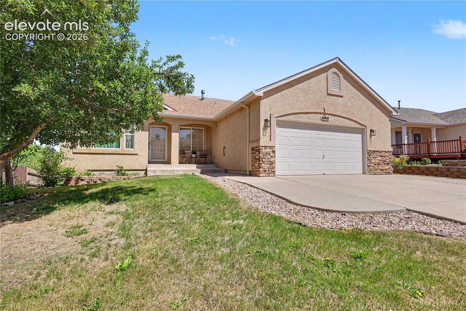 Front exterior featuring stucco siding, stone accents, an attached garage, a concrete driveway, and a front patio