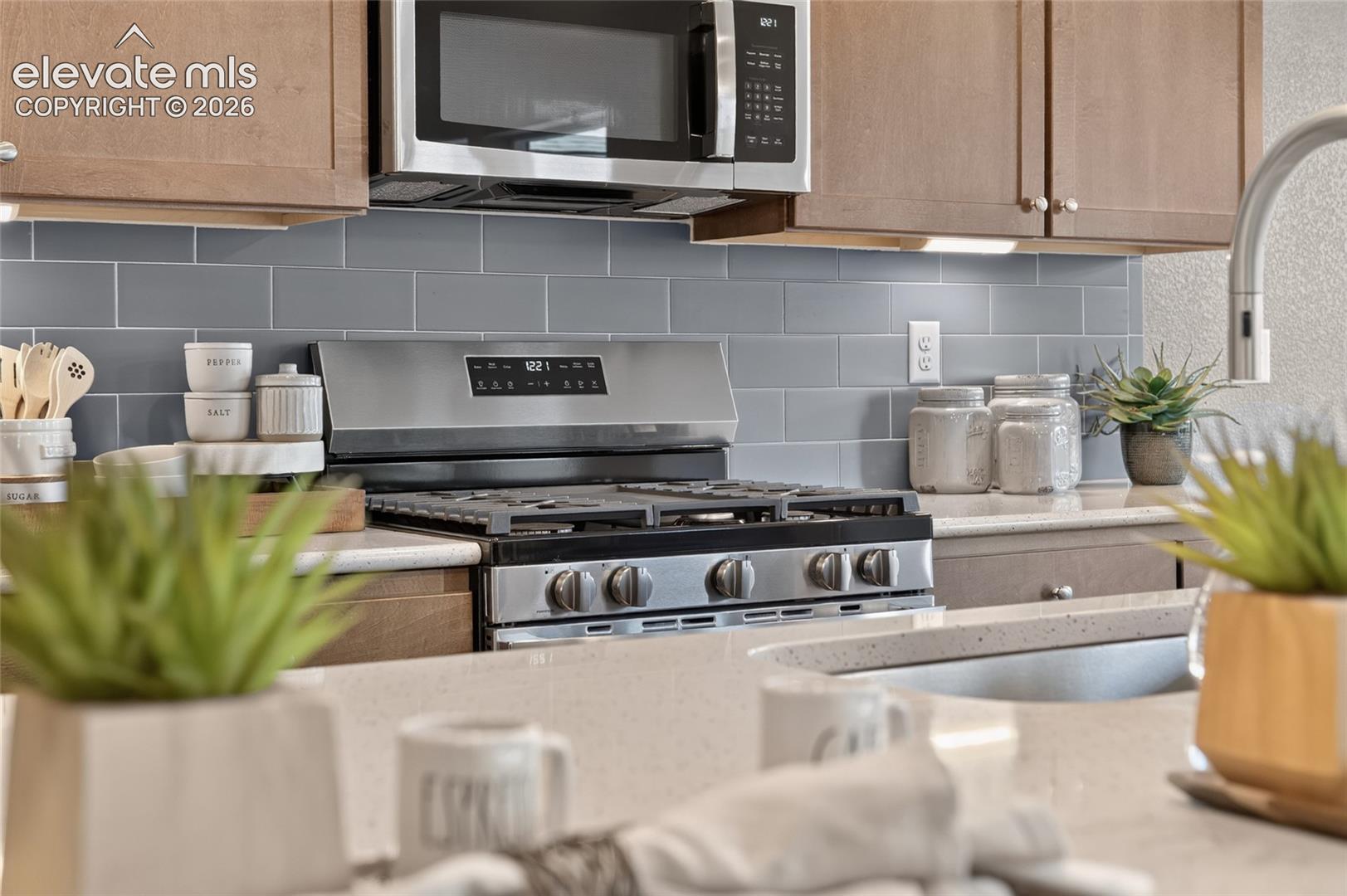 Kitchen featuring wood-finish cabinetry, stainless steel gas range, built-in microwave, grey subway tile backsplash, and composite countertops