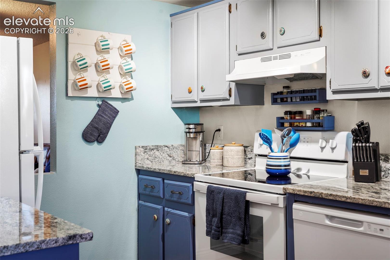 Kitchen featuring stone countertops, two-toned cabinetry, an electric range, and a built-in range hood